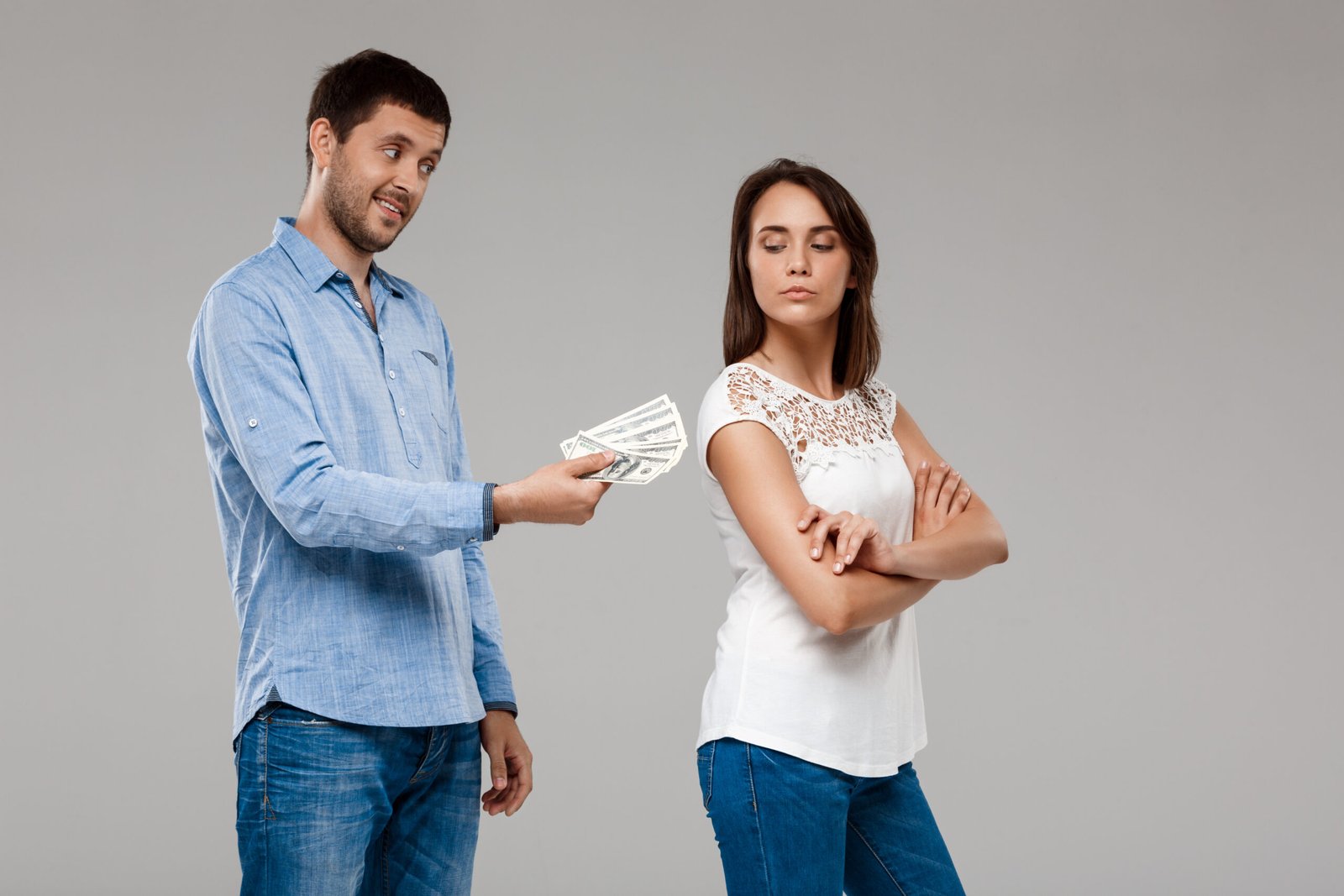 Young handsome man giving money to woman, smiling over grey background. Copy space.